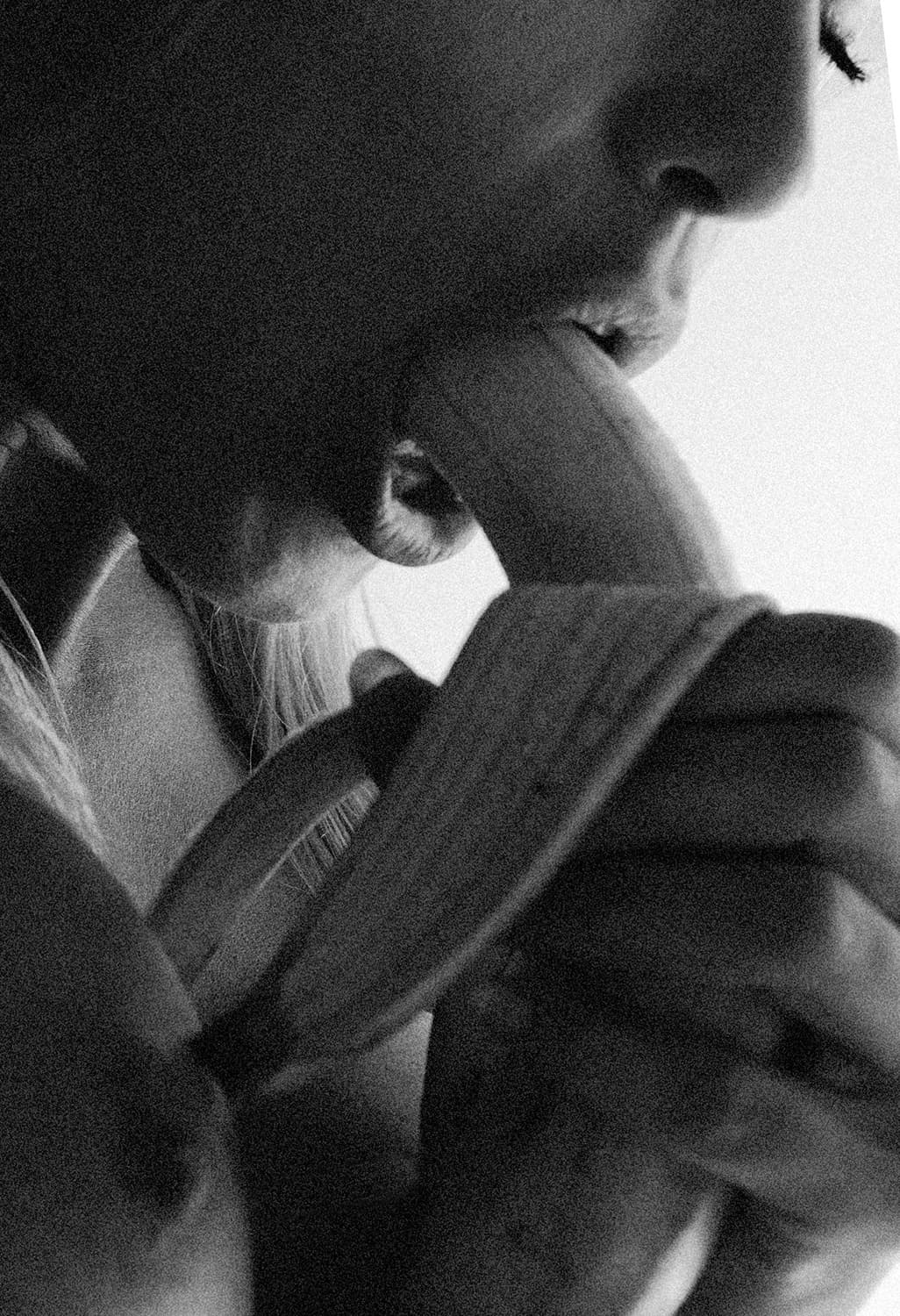 Eine körnige Schwarz-Weiß-Fotografie zeigt eine Frau, die eine teilweise geschälte Banane mit den Lippen berührt. Der Fokus liegt auf ihrem Mundbereich, während ihre Hand die Banane hält. Das Bild hat eine starke Kontraste und eine grobe Körnung, die an analoge Filmaufnahmen erinnert