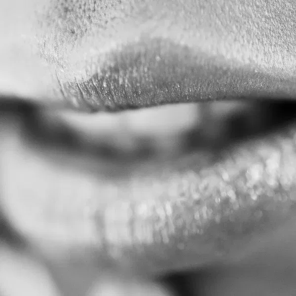 Erotische Fotografie einer Nahaufnahme von Lippen, die in sanften Licht- und Schattenverhältnissen dargestellt wird, was eine subtile, verführerische Atmosphäre schafft.