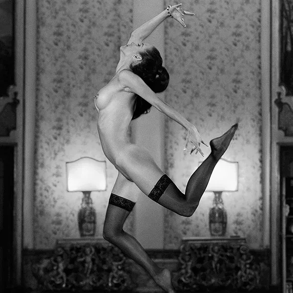 Erotic photography: A naked woman in sexy stockings dances in an elegant room and leaves gravity behind, the focus is on dynamic movement and sensual elegance.