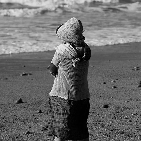 Artistic street photography of an elderly woman by the sea, lost in thought.