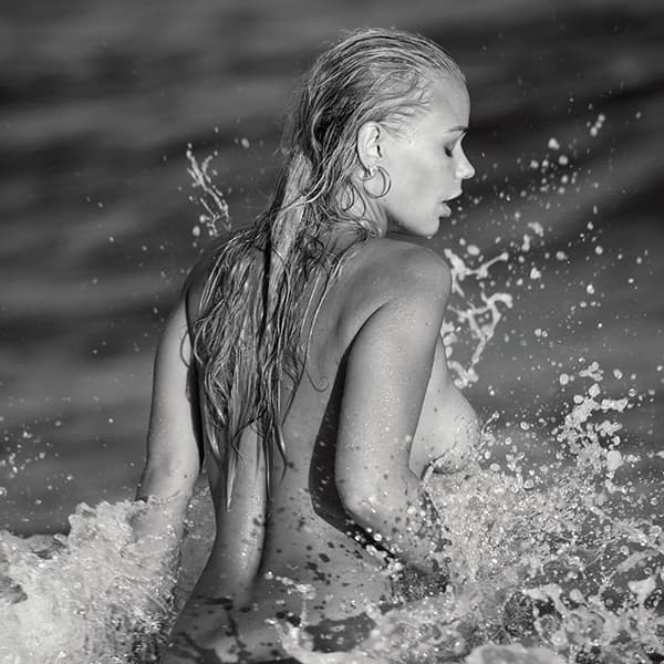 Limitierte Fine Art Fotografie: Nacktes Model mit nassen Haaren in den aufspritzenden Wellen, eingefangen in kraftvollem Schwarz-Weiß.
