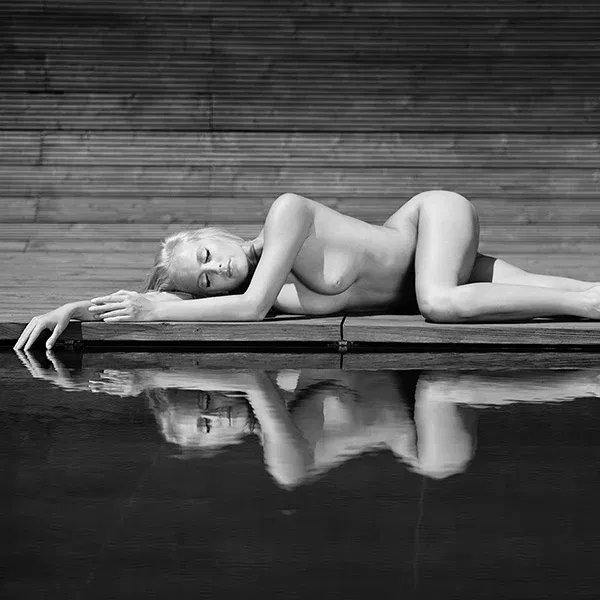 Frau liegt nackt am Beckenrand mit Spiegelbild im Wasser – erotische Aktfotografie.