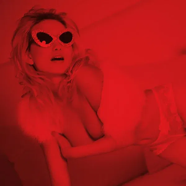 Erotische Aktfotografie einer Frau im roten Licht mit Herzbrille und lasziver Pose
