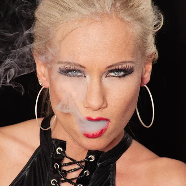 Erotische Fotografie einer Frau im schwarzen Outfit, die mit roten Lippen und intensivem Blick in die Kamera schaut.