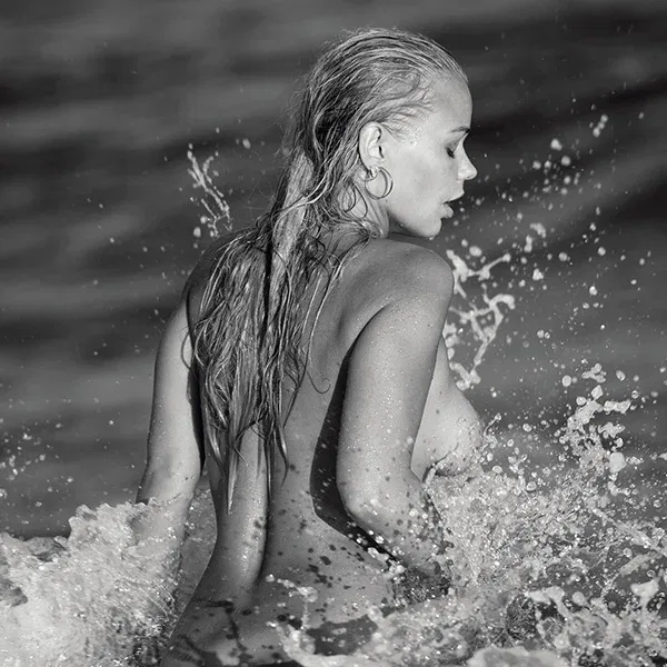 Limitierte Fine Art Fotografie: Nacktes Model mit nassen Haaren in den aufspritzenden Wellen, eingefangen in kraftvollem Schwarz-Weiß.